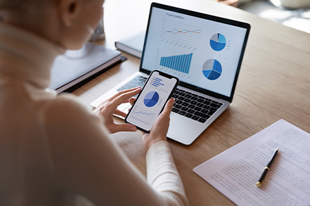 Woman looking at various graphs on phone and computer