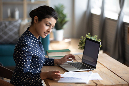 Woman looking at papers while typing on a laptop